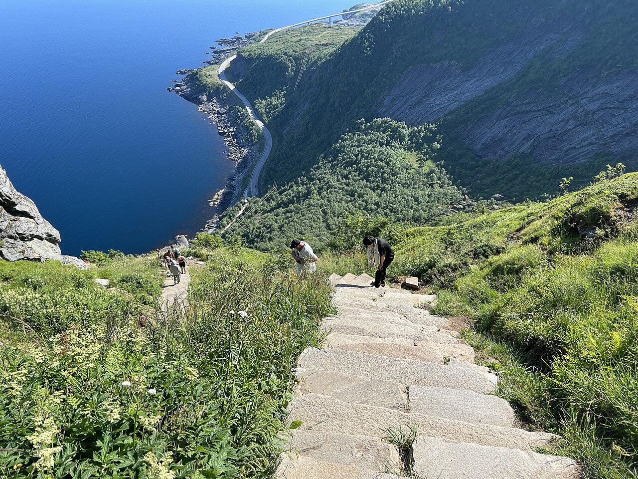 Hikers on the stone steps of the Reinebringen trail above the blue sea in Lofoten